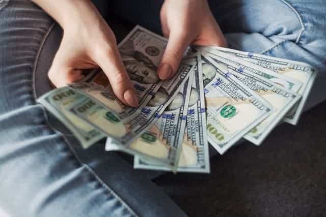 Close-up of a person's hands holding a spread of hundred-dollar bills