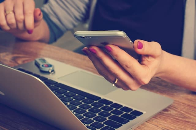 Woman using a smartphone with a laptop and car keys in the background. 